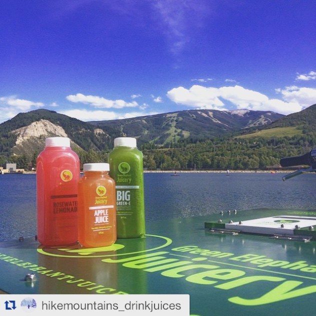 Three bottles of juice on the lid of an ice cream bike in the foreground and a beautiful landscape shot of a lake and mountains in the background