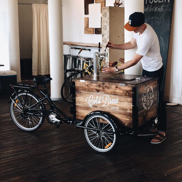 Man in t shirt and ball cap pours Cold Brew Coffee from the tap on the coffee bike box