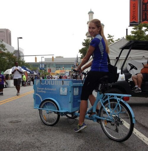A woman riding an Icicle Tricycles Experiential Marketing Cargo Bike with custom powder coat frame at a street fair
