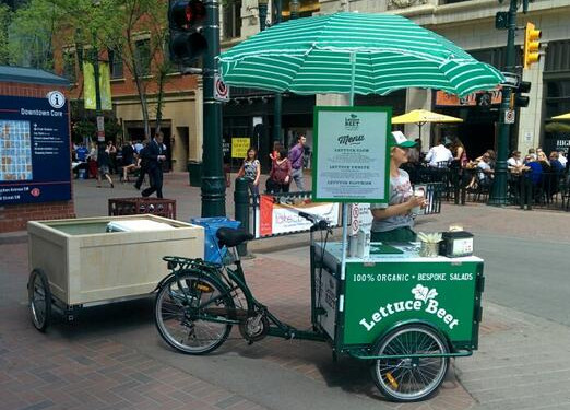Icicle Tricycles Food Bike with a green and white striped umbrella branded for LettuceBeetYYC Salad's food bike business vending tricycle popup in a busy city space