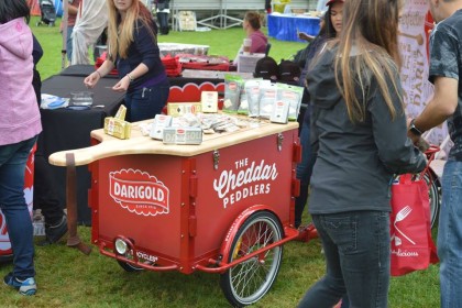 A red Darigold branded marketing Cargo bike with a custom lid shaped like a giant cutting board with a full spread of butter and cheese at a marketing event