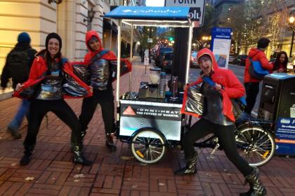 A group of stoked peddlers posing next to their coffee Custom Cargo Bike parked on the sidewalk in a major city