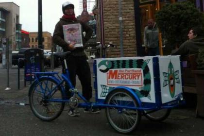 a man delivering news papers using an Icicle Tricycles Newspaper Delivery Bike branded for the Portland Mercury 
