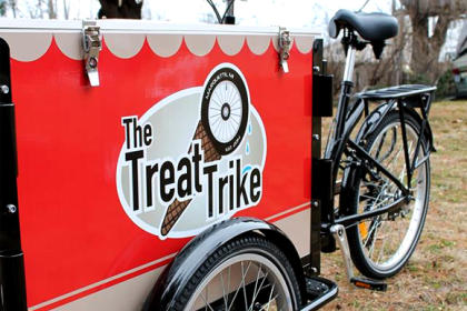 An Icicle Tricycles Ice Cream Cargo Bike branded for The Treat Trike parked in a back yard