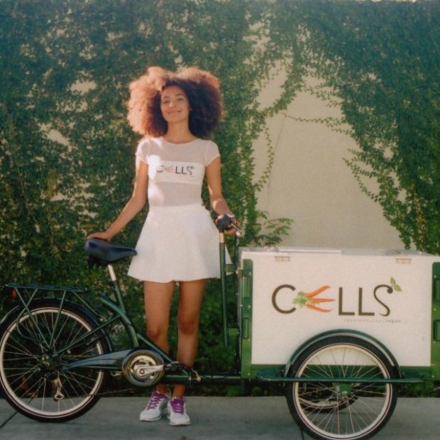 an icicle tricycles food bike branded for cells sprouted raw vegan foods and a person in front of a wall of vines