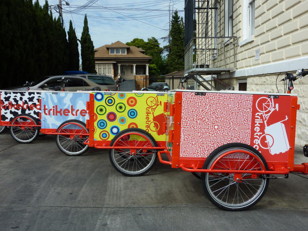 A fleet of Icicle Tricycles marketing custom branded Ice Cream Bikes with red frames in an alley way on a sunny day.