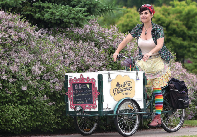 Mrs Delicious riding an ice cream tricycle bike through a park