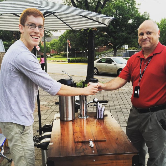 Barista serving a customer from a vinyl wrapped icicle triycle coffee bike in a park