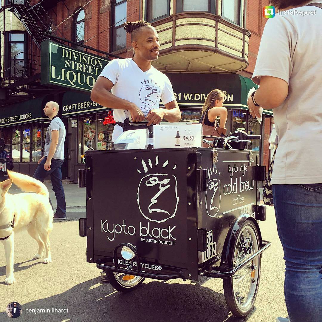 barista serving coffee in a town square from an Icicle Tricycles Cold Brew Coffee Bike