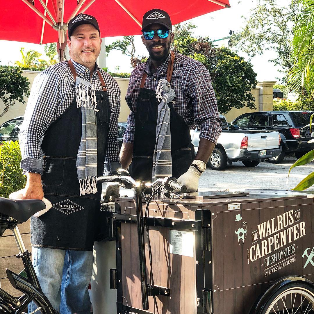 Two Rockstar caterers with faux wood vinyl wrap The Walrus and carpenter oyster Icicle Tricycles Ice Cream Bike Vending cart on a sunny day